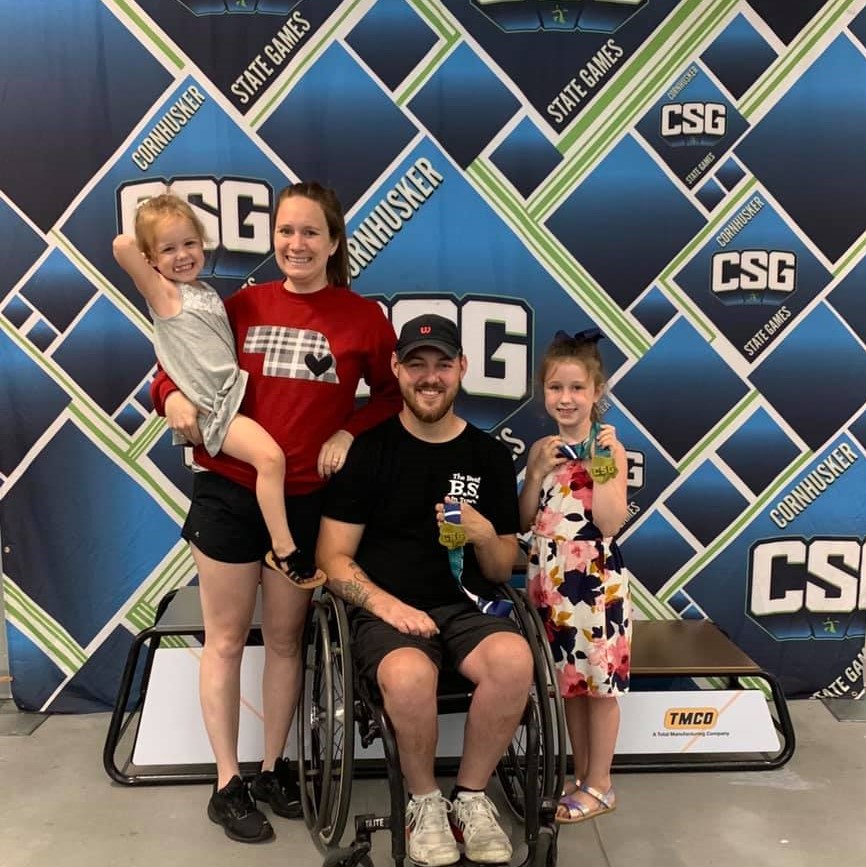 A man in wheelchair posing with is wife and two young kids at the CSG wheelchair awards
