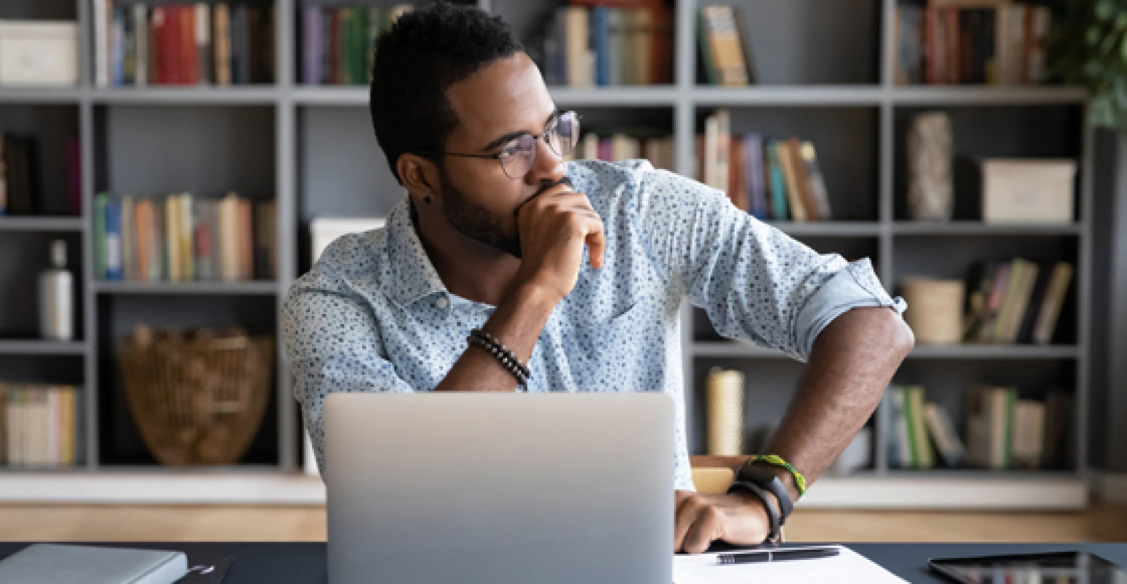 A man sitting behind his laptop looking off to the side lost in thought