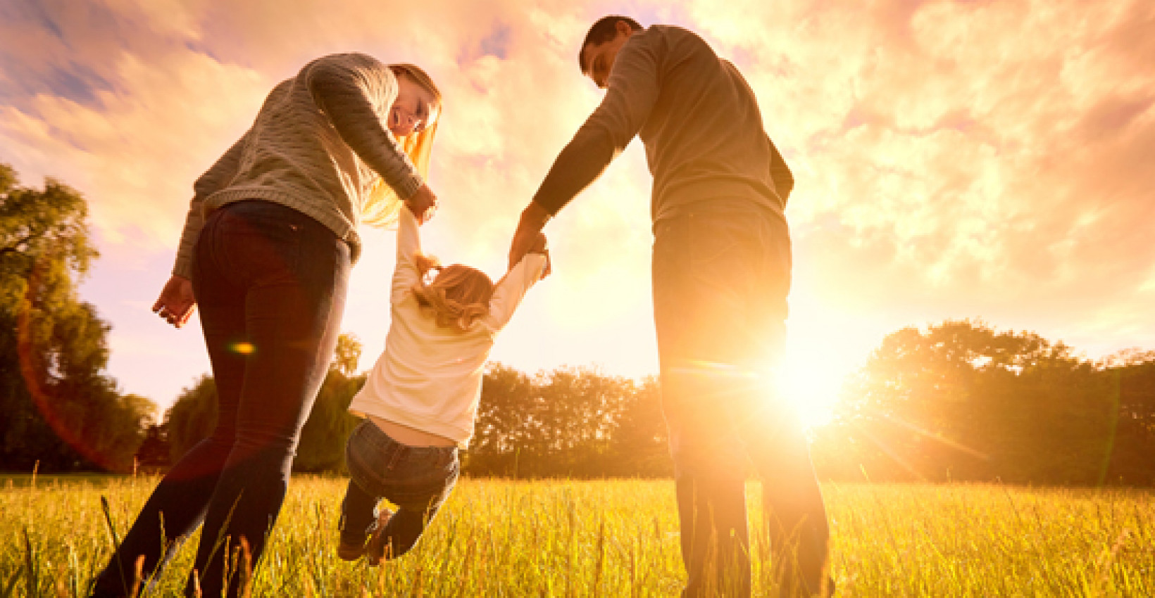 A couple swinging a child by the arms between them at sunset