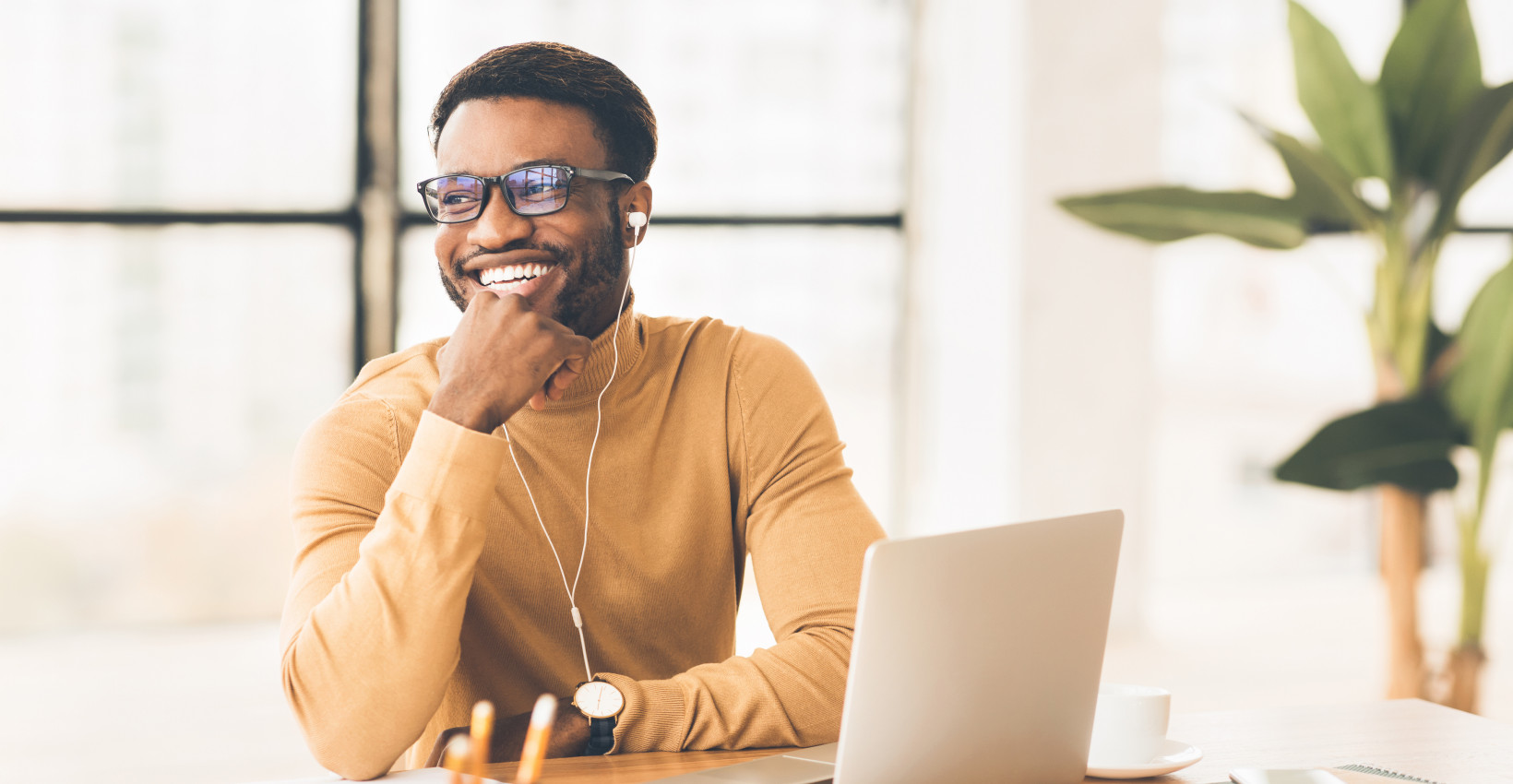 A man smiling as he sits at his home desk with a laptop