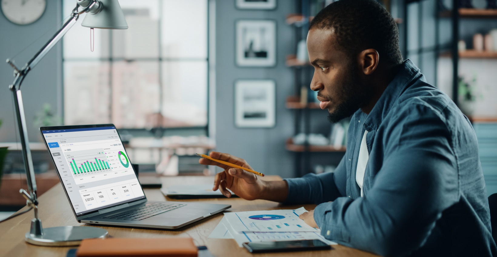 A man sitting at a wooden desk looking at charts on his computer. 