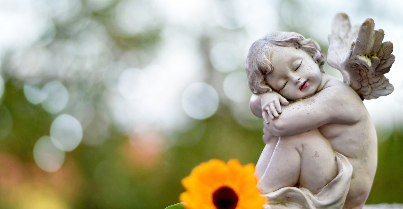 a concreate angel sits next to a flower