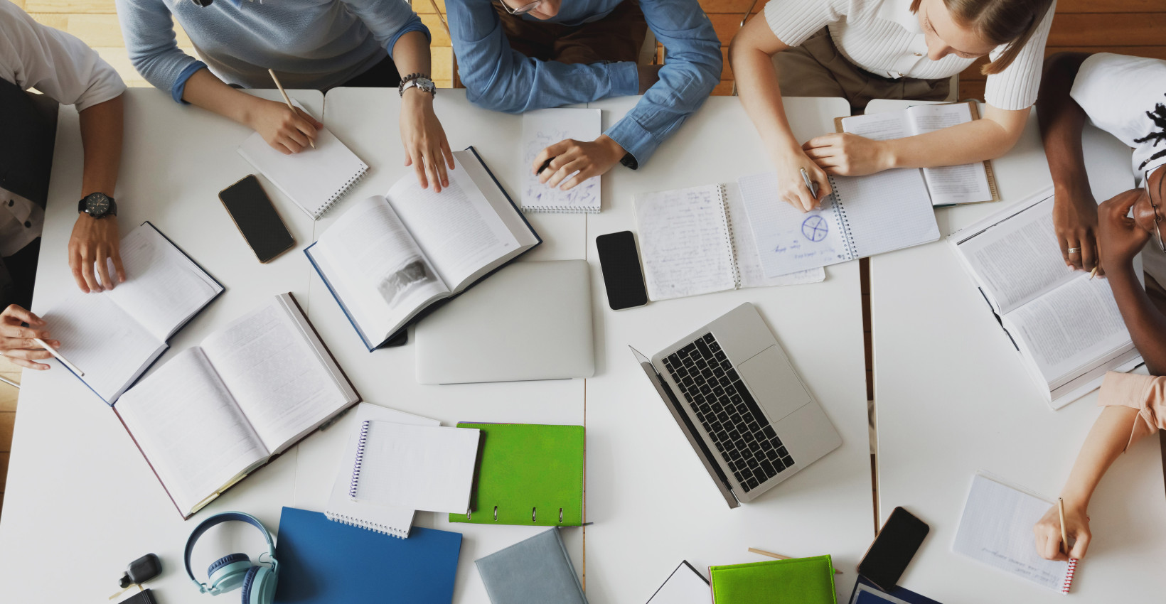 a group of people sit around a table with computers, papers, and pencils 
