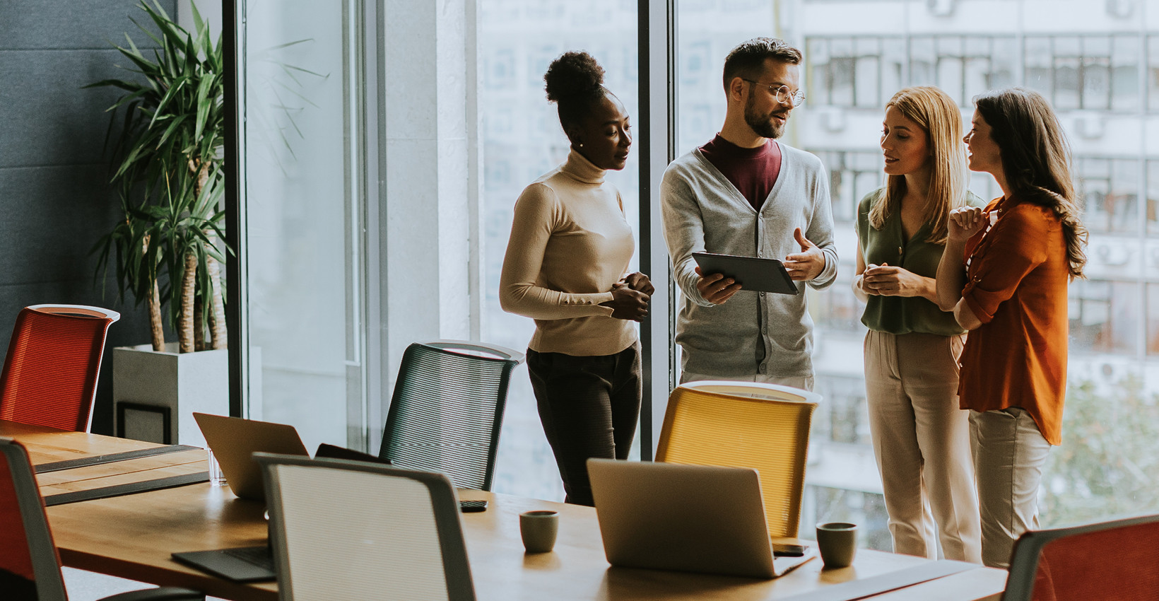4 people stand near a window in a conference room looking at a tablet