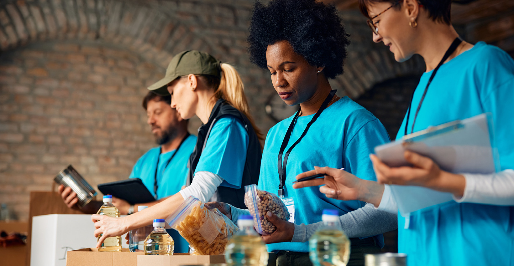 four people wearing blue shirts stand at a table packaging food items