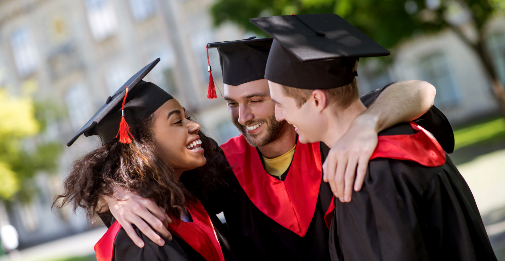 three college graduates stand together smiling