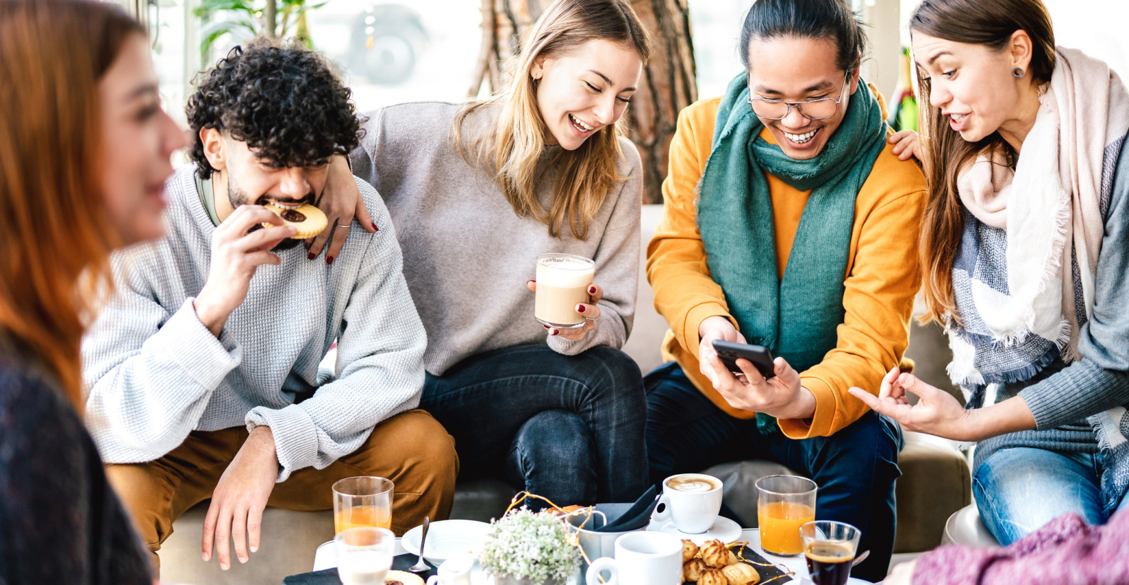 a group of 5 young people sit around a table with snacks and drinks laughing
