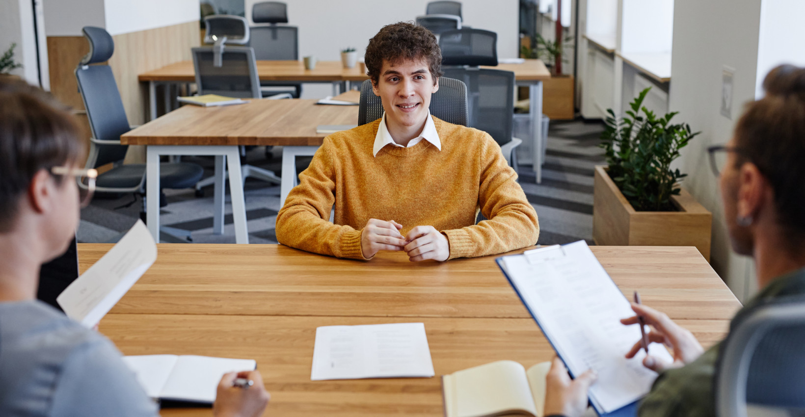 a young man sits nervously across from two older people during a job interview