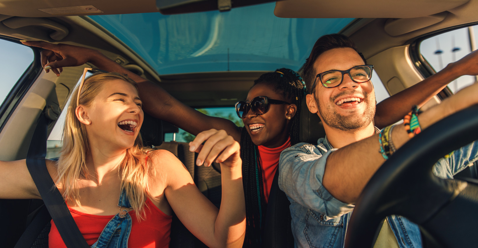 three younger people drive in a car together laughing