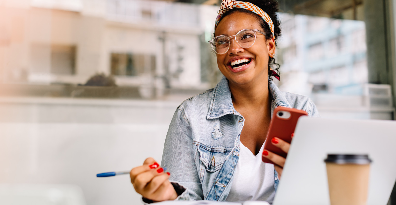 a young black woman smiles while sitting at a table with a laptop and coffee