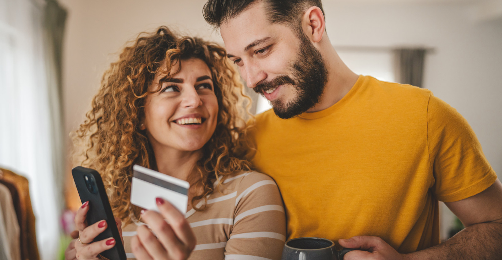 a happy couple stands together holding a debit card