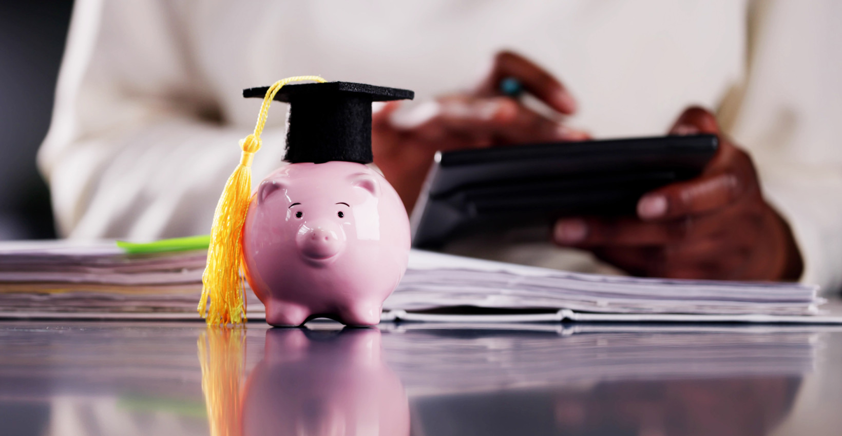 a pink piggy bank sits on a desk with a college graduation hat on