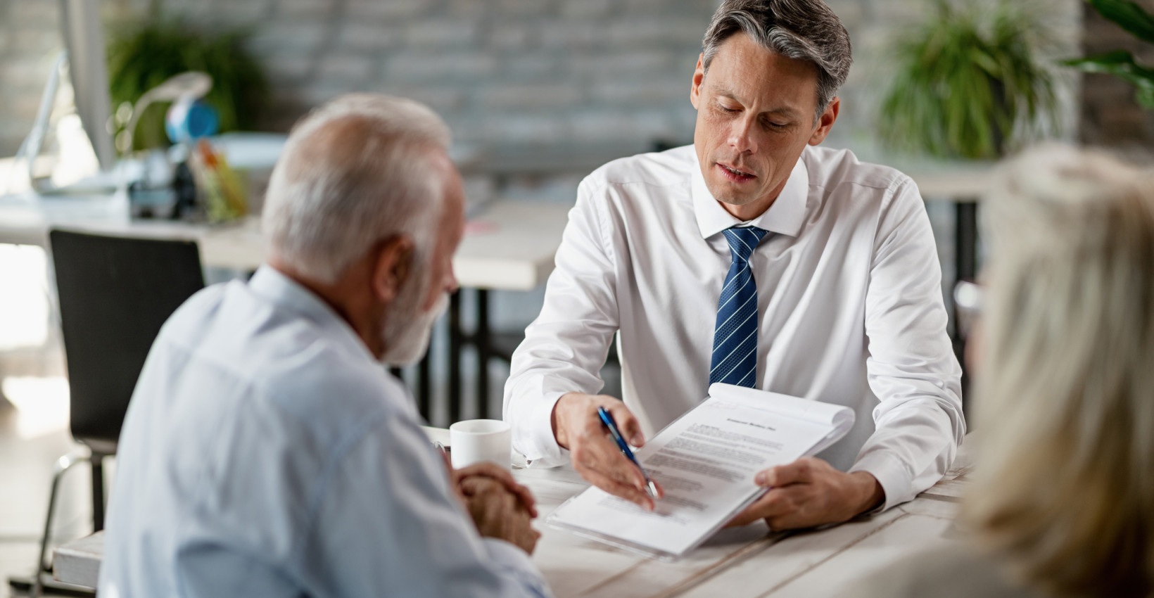 an older couple sit with a younger man at a desk mid conversation