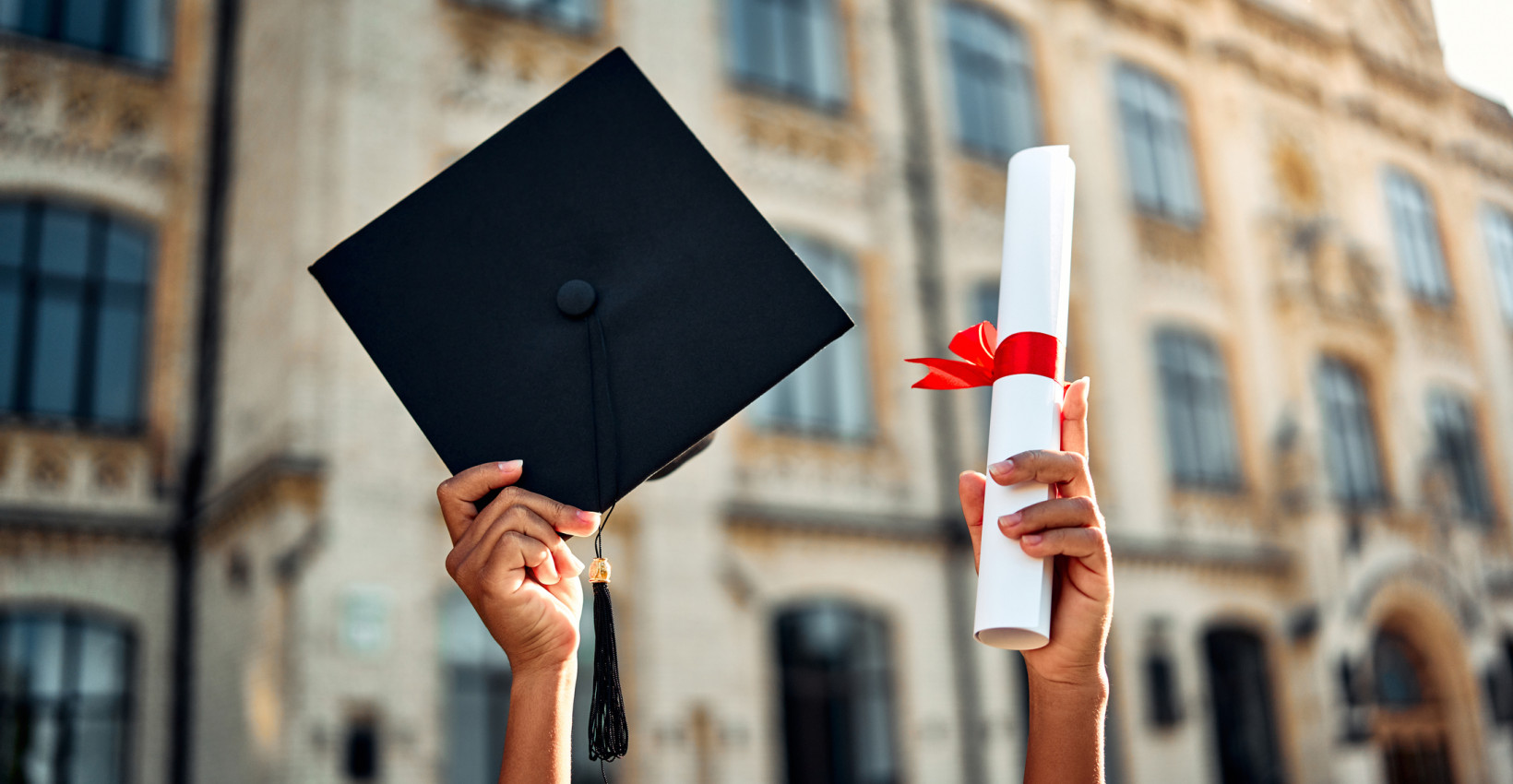 a person holds up a graduation hat and diploma wrapped in red ribbon