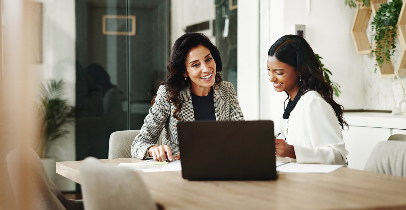 two women sit behind a laptop together smiling