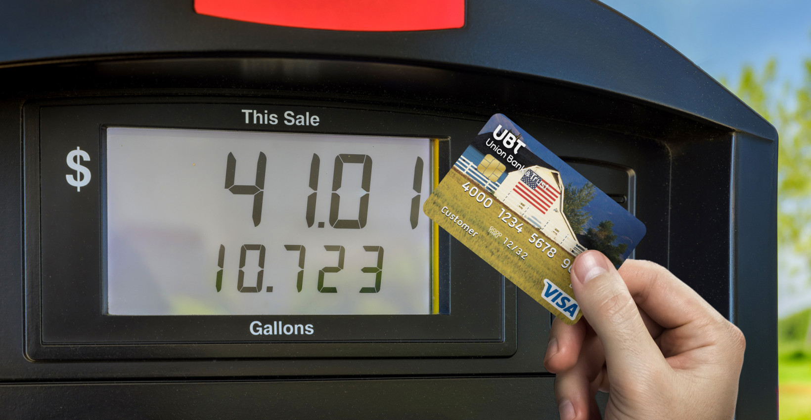 a person holds their ubt debit card up next to a gas pump