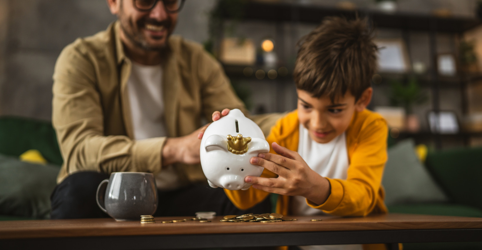 a dad and son dump out a piggy bank onto a coffee table