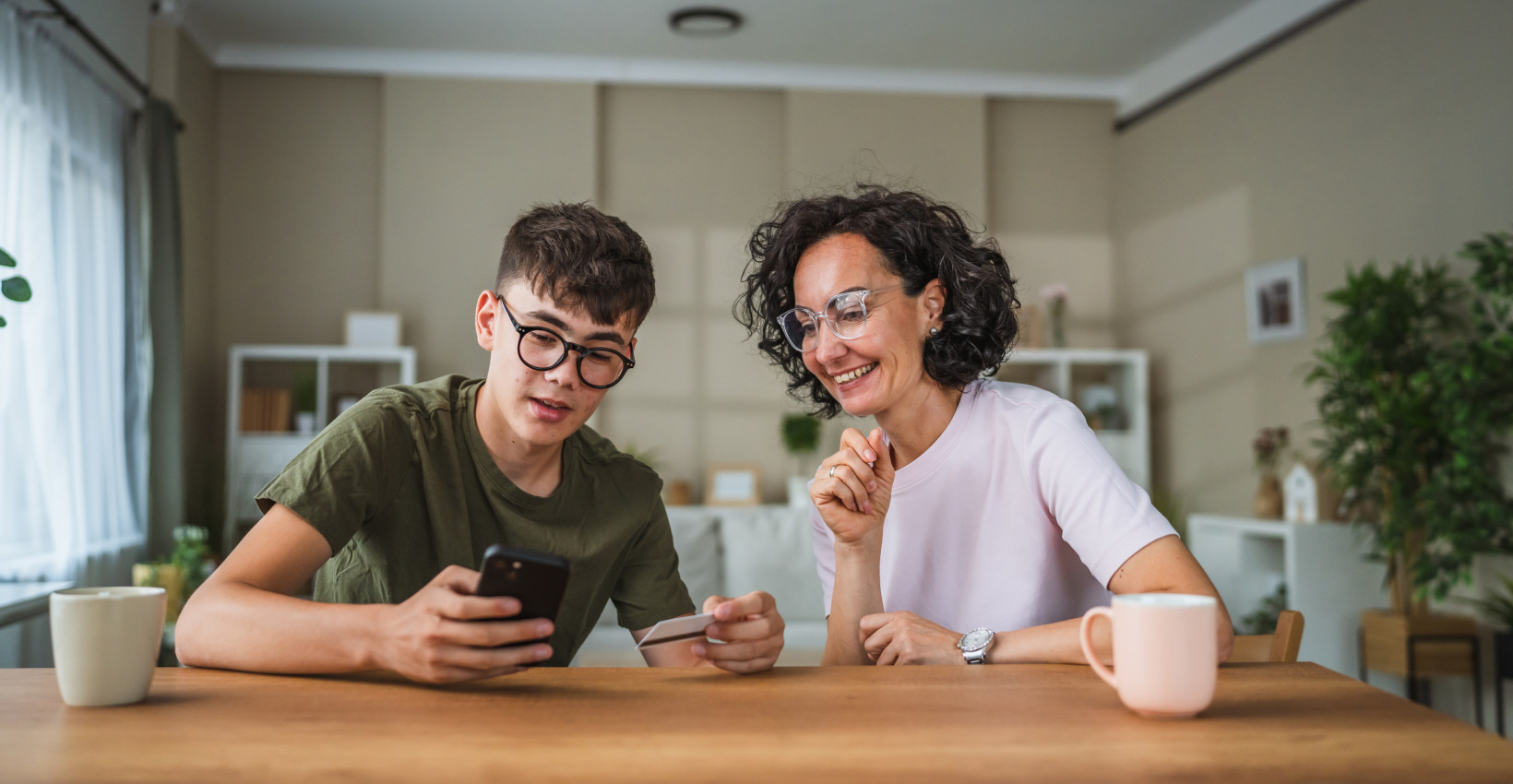 a mom and son sit at a table looking at a phone together