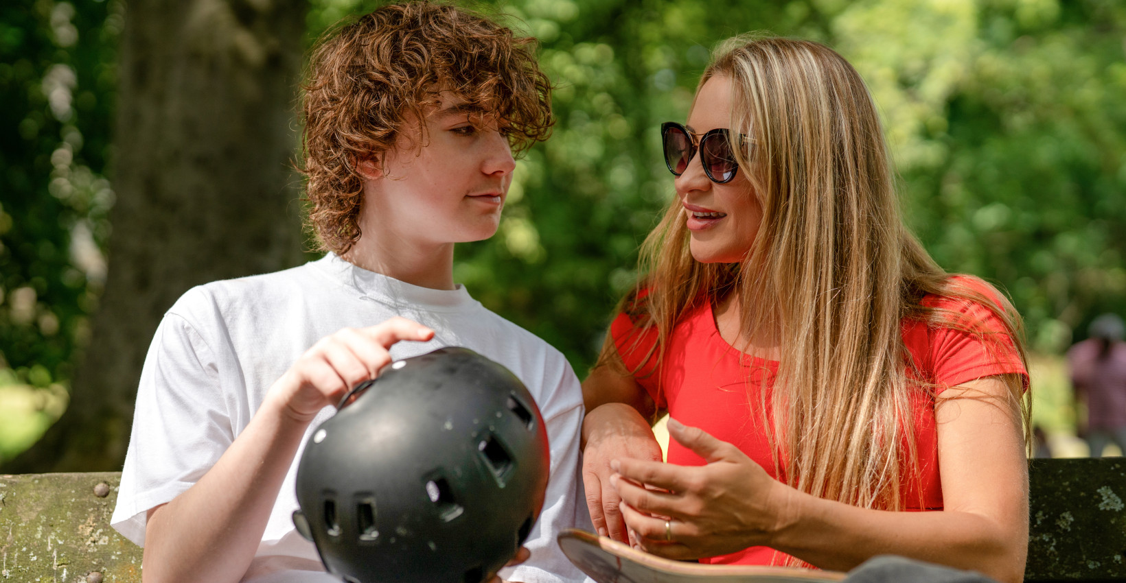 a mom and son sit on a bench at a skatepark