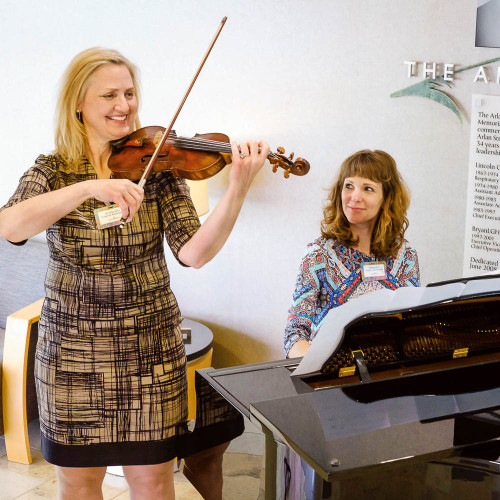 Two women playing violin and a piano. 