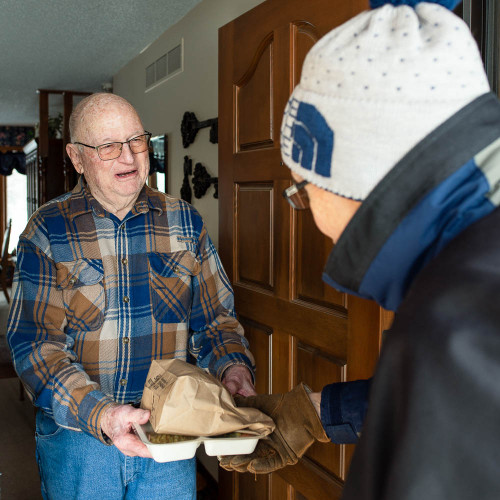 A volunteer handing food to an elderly man. 
