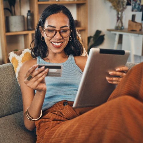 A woman smiles as she looks at her credit card and tablet