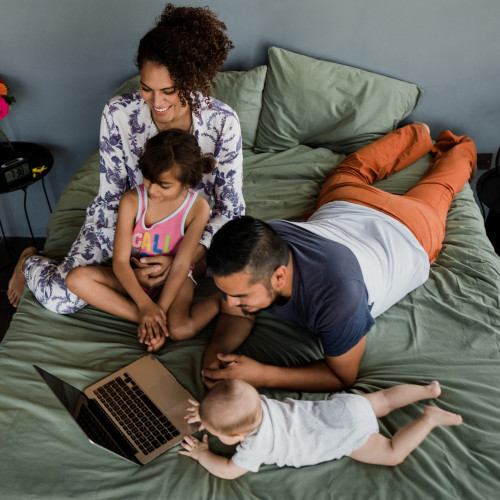A family gathers around a laptop to watch a show while in bed
