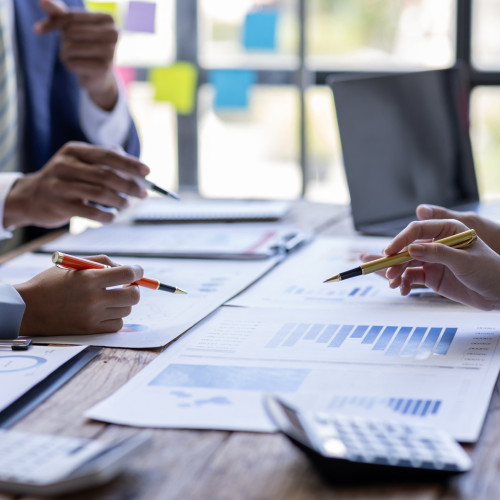 Three sets of hands holding pencils over documents on a desk