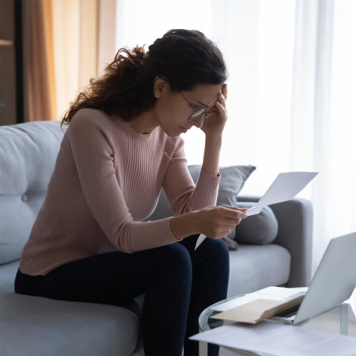 A woman on the couch looking concerned at a sheet of paper