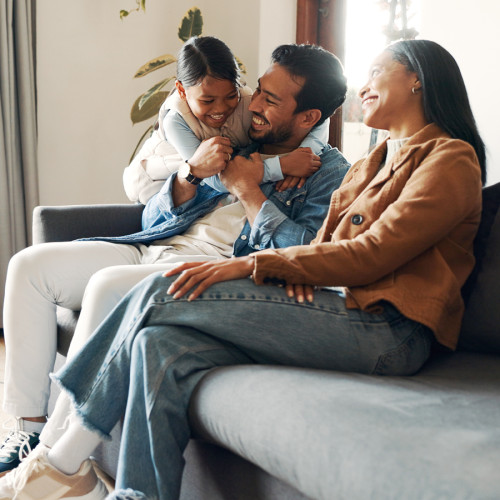 a man, woman, and small girl child sit on a couch laughing