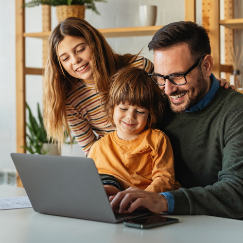 a man, woman, and girl child sit together looking at a laptop