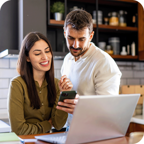 A couple looking at a phone in front of a laptop