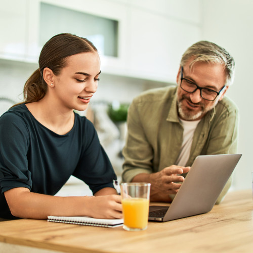 A dad and daughter look at a laptop on the breakfast table