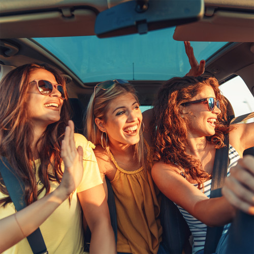 Three teen girls looking out the driver's window in a car