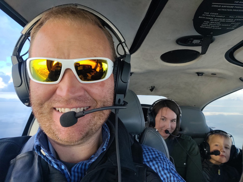 A selfie of a pilot in a small plane with a mother and young child behind him