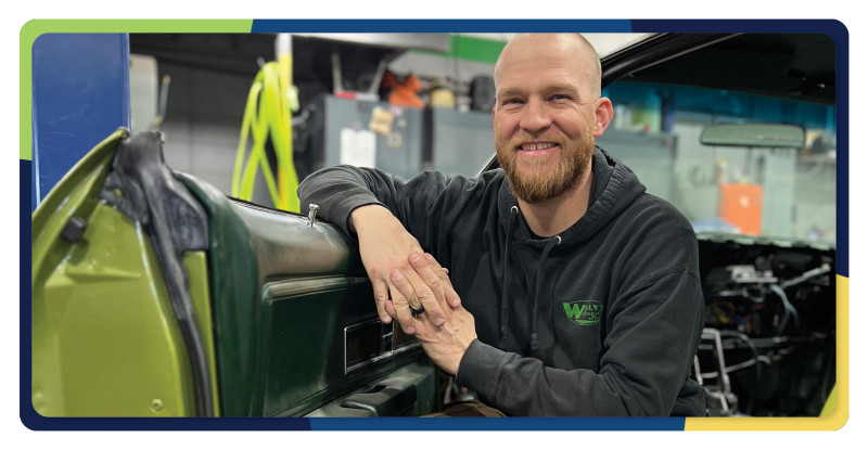 Wally sits in a car with the door open smiling