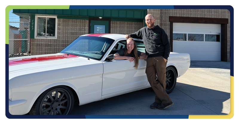 Miriam sits inside a whit 2 door car while Wally leans on the door smiling