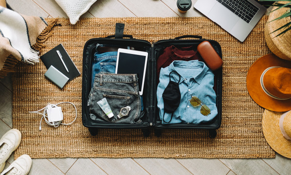 A suitcase neatly packed with jeans, sunglasses, and a hat. 