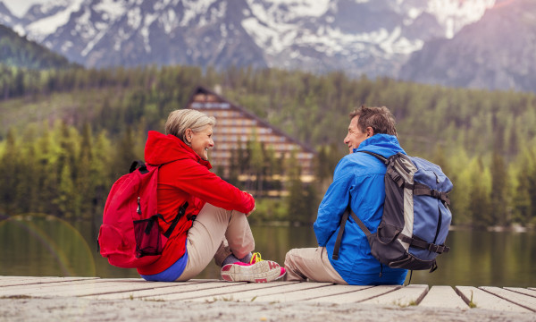 A middle aged man and woman sitting by an alpine lake after a hike