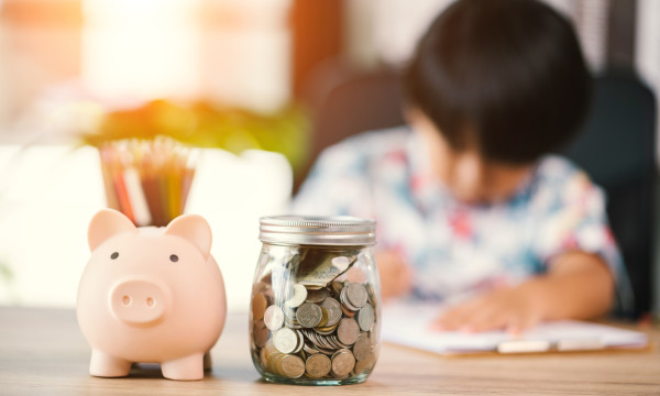 a small child sits at a table with a piggy bank and money