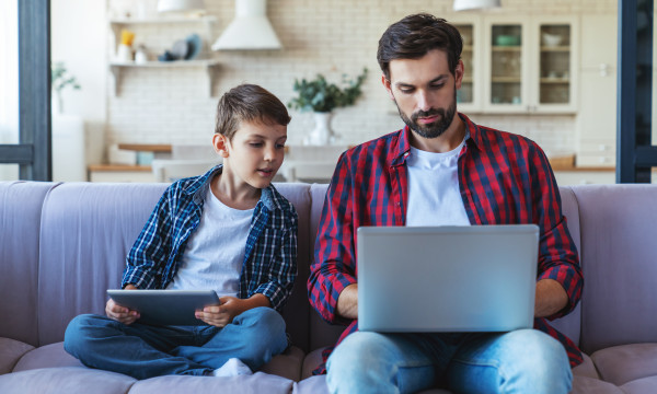 a father and son sit together on a couch looking at a laptop