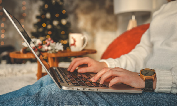 a person sits on a couch with a laptop on their lap with christmas decorations in the background