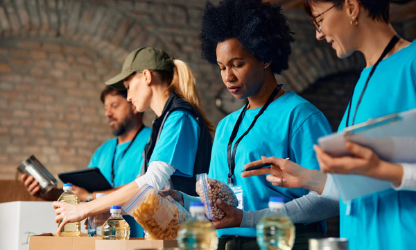 four people wearing blue shirts stand at a table packaging food items