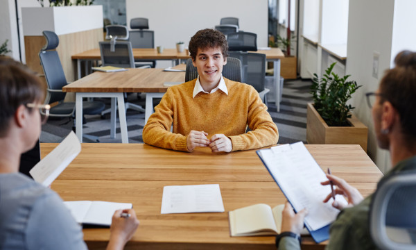 a young man sits nervously across from two older people during a job interview