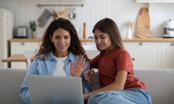 a mother and daughter sit on a couch looking at a computer together