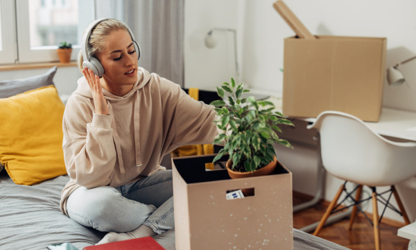 a younger female sits on a bed with headphones on looking through a box