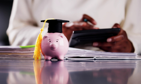 a pink piggy bank sits on a desk with a college graduation hat on