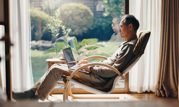 a man sits in a rocking chair by a window with his laptop