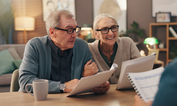 an elderly couple sits at a table reviewing paperwork