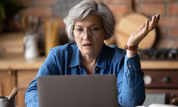 an older woman sits at her computer with a frustrated expression